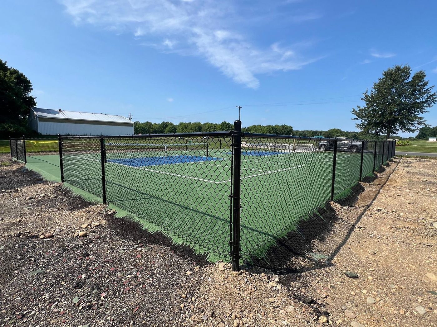 Chain-link fenced outdoor sports court with green turf and blue lines under a clear sky