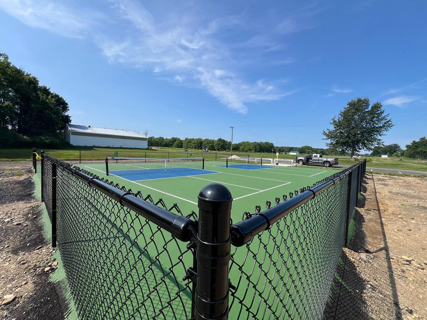 Fenced outdoor tennis court with blue and green playing surface under a clear sky