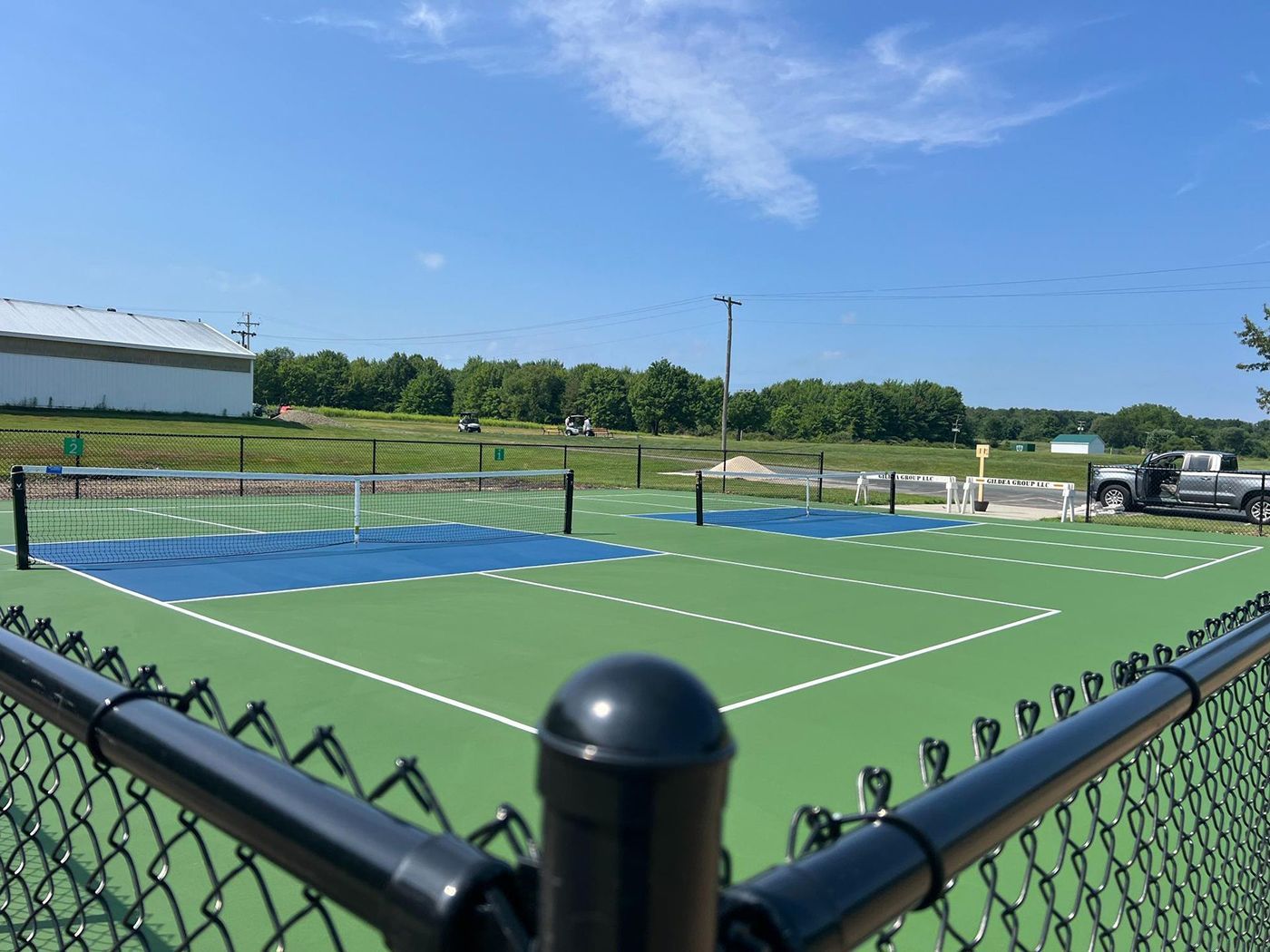 Outdoor tennis courts with green and blue surfaces behind a black fence on a sunny day
