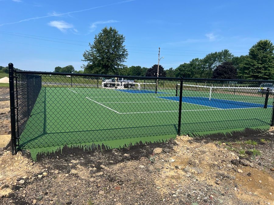 Chain-link fence around an artificial turf sports field under a clear blue sky.