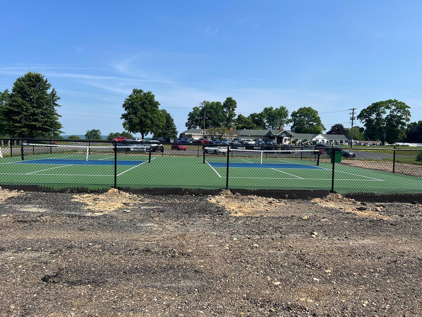 Outdoor sports field with green turf, chain-link fence, and trees under a clear blue sky