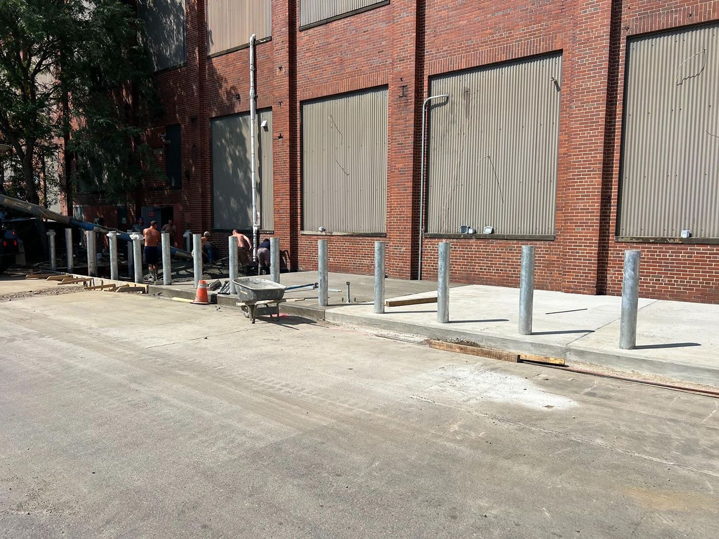 Brick building with boarded windows, sidewalk bike rack, and a row of short metal bollards along the curb