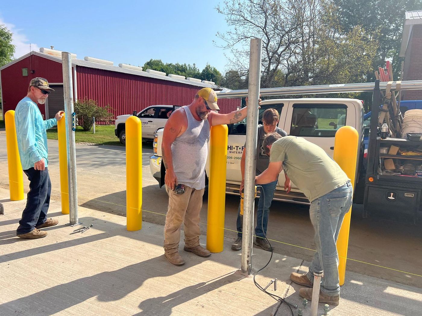 Workers install a metal post between yellow bollards outside a building