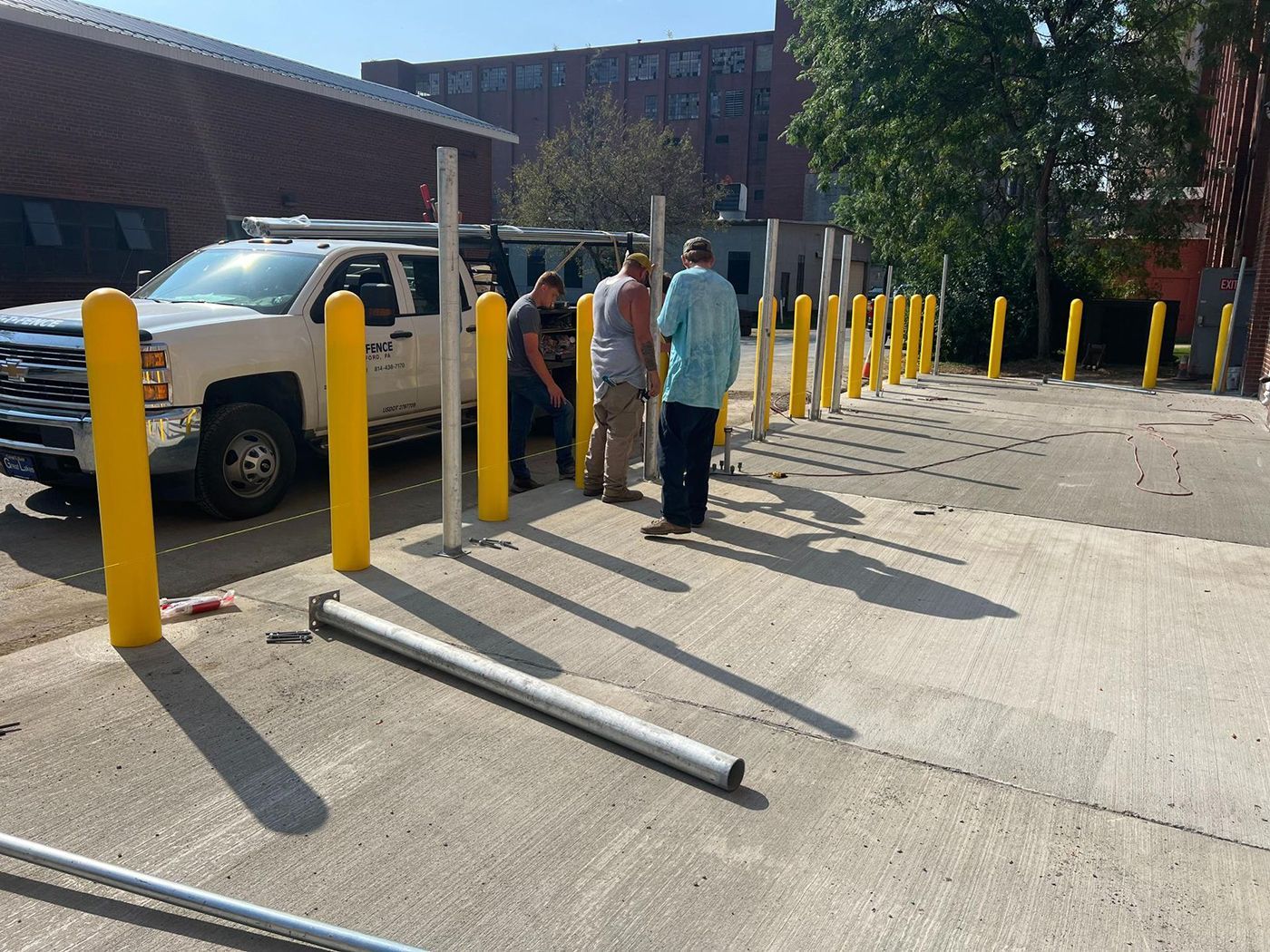 Yellow bollards line a parking lot walkway near a white truck and two people under a building awning.