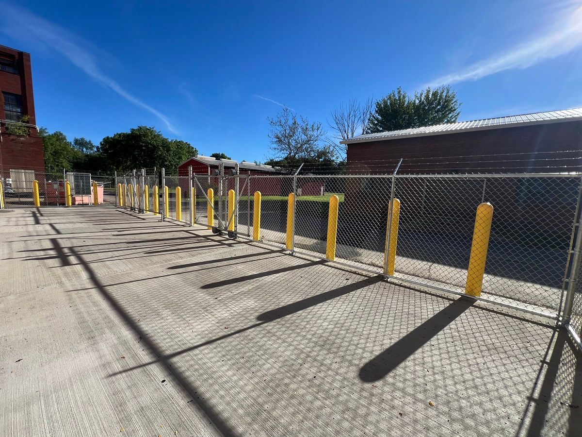Empty paved lot with yellow bollards and chain-link fence under a clear blue sky