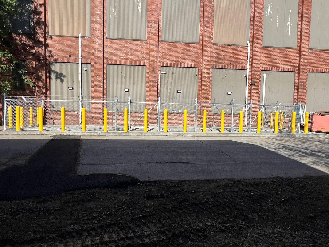 Yellow bollards line a sidewalk in front of a brick building with boarded windows and a dark asphalt foreground.