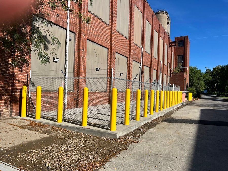 White sliding gate in front of two industrial buildings on a gray concrete surface, blue sky in background.