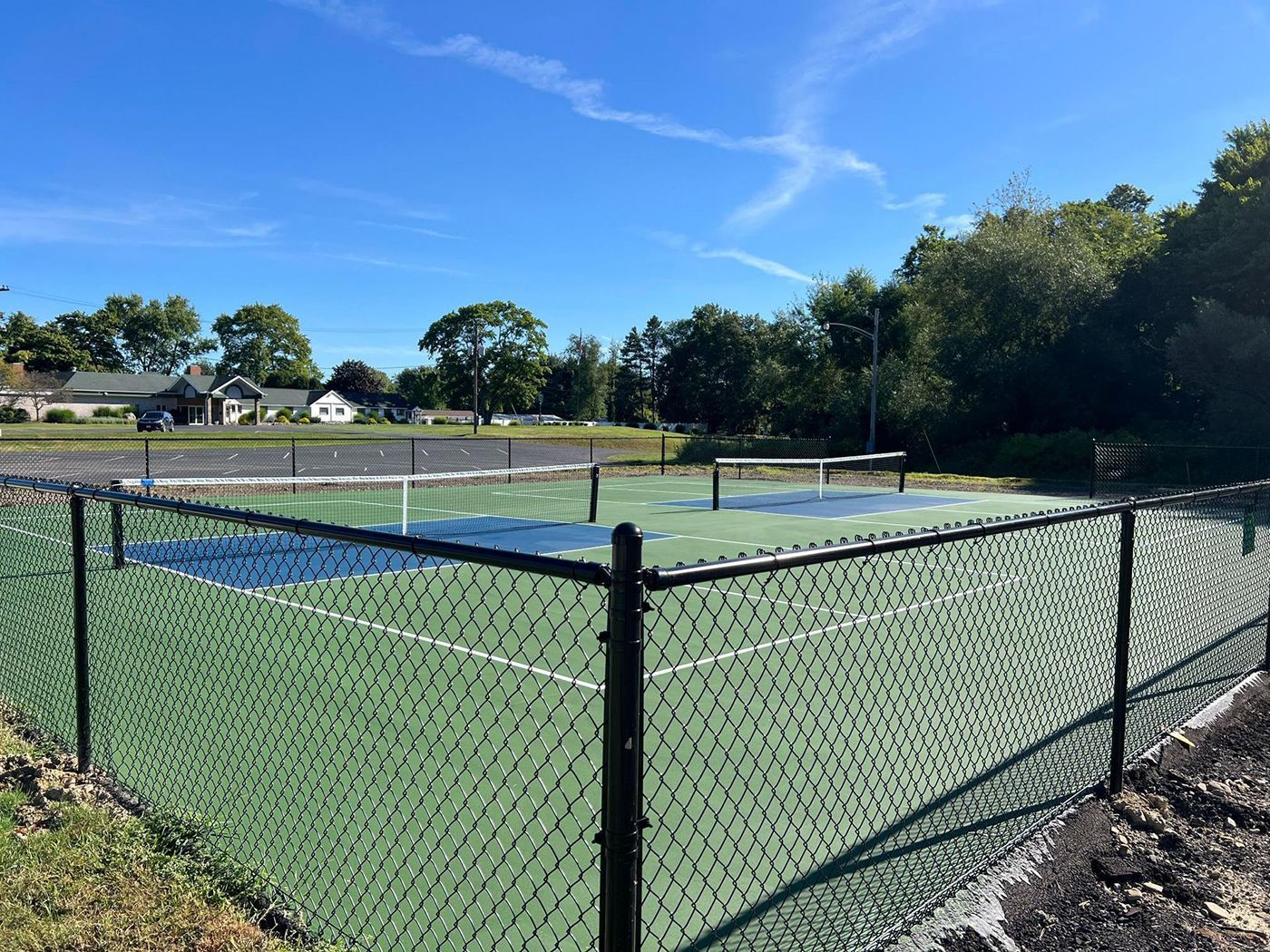 Chain-link fenced outdoor pickleball court with blue and green surface under a clear sky