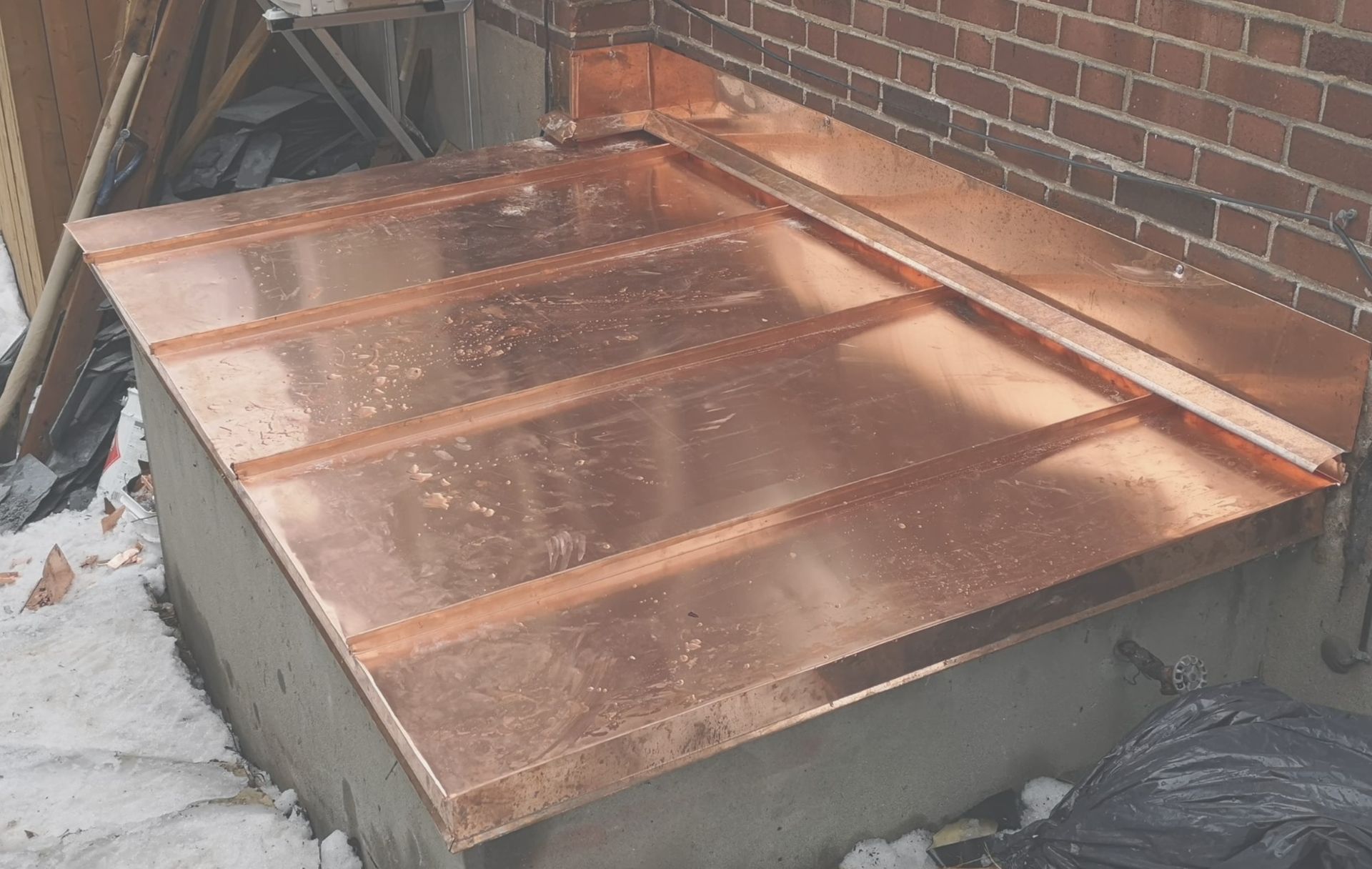 A copper roof is being installed on the side of a brick building.