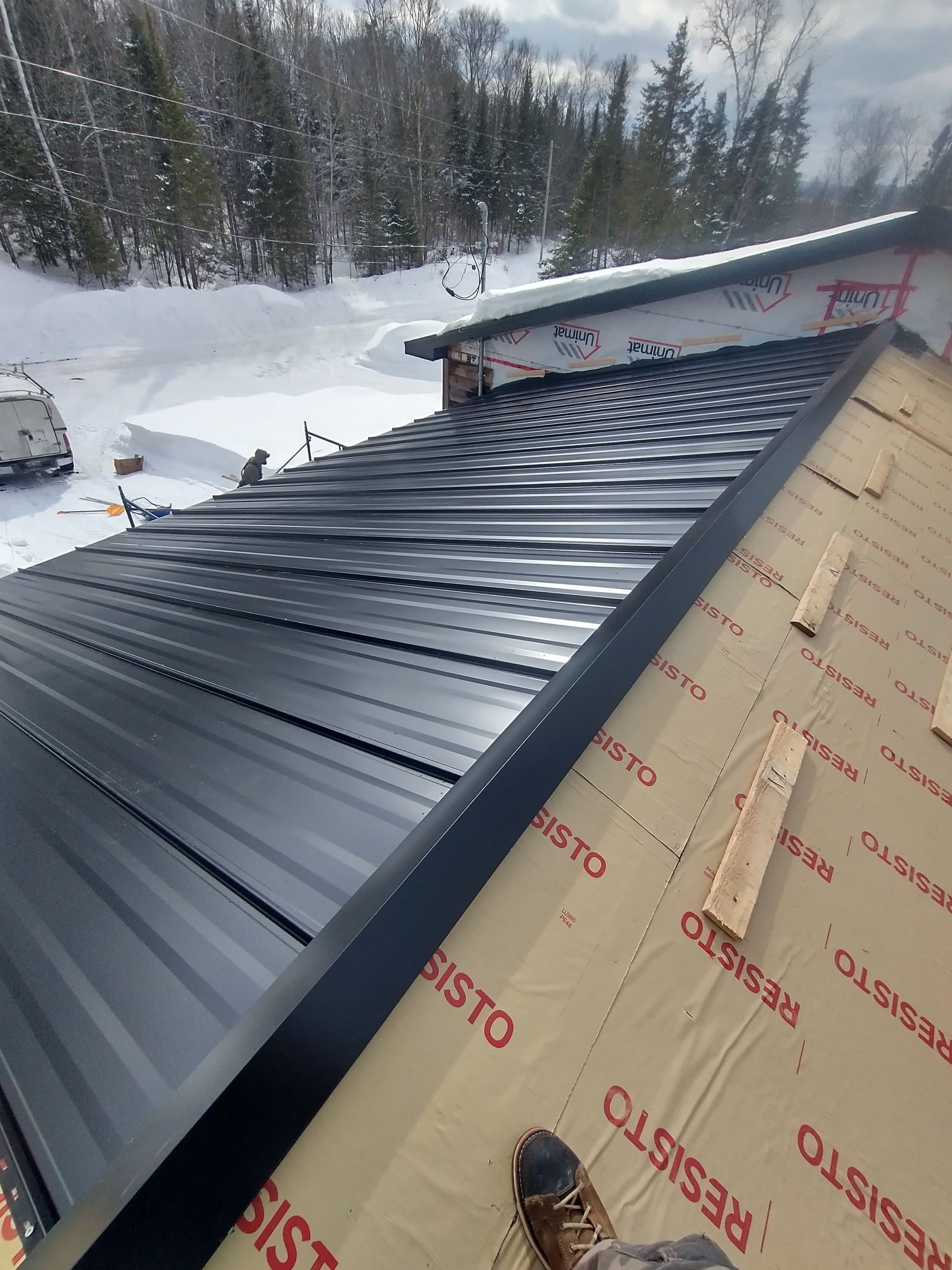 A black metal roof is being installed on a house