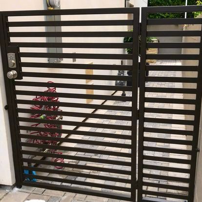 A wrought iron gate is sitting on a brick sidewalk next to a building.