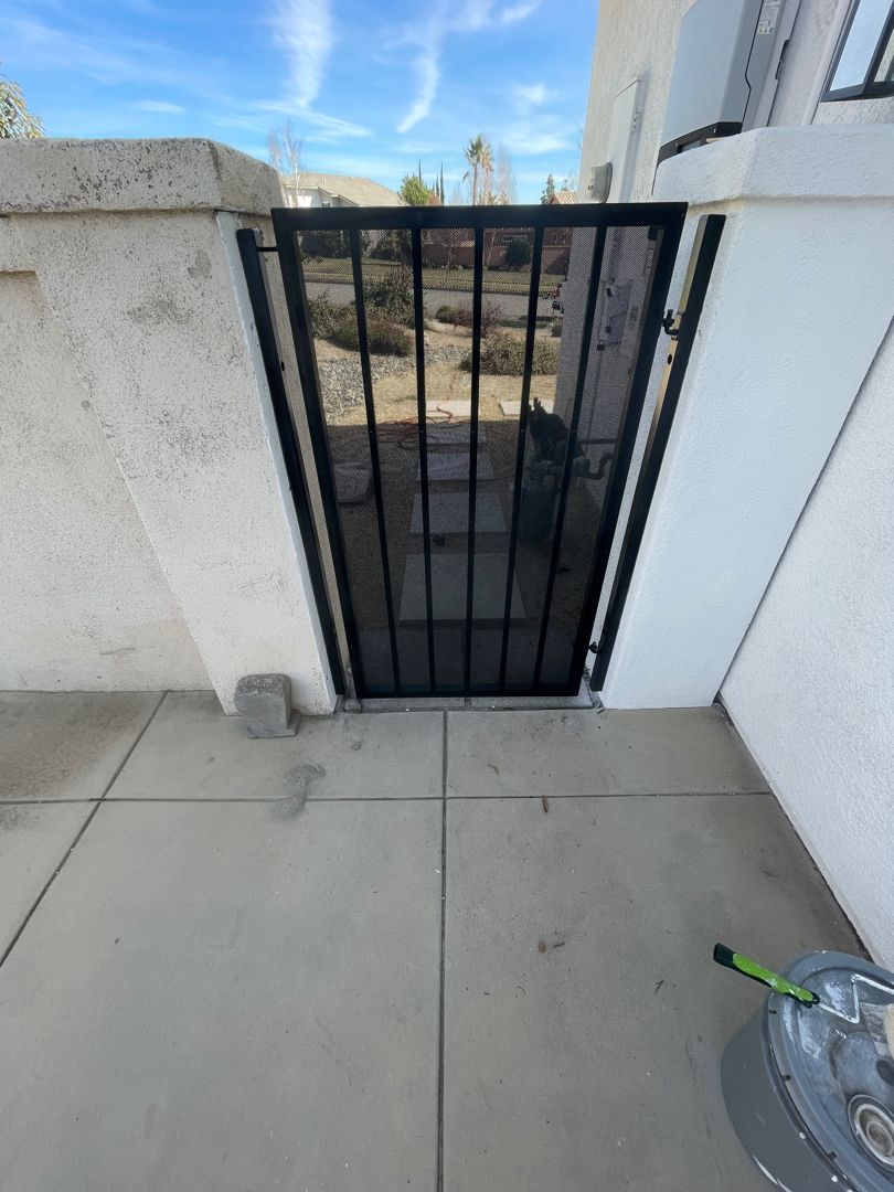 A black gate is sitting next to a white wall.