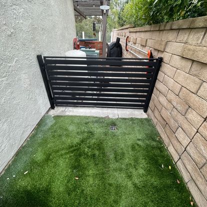 A black gate is surrounded by a brick wall and a lush green lawn.