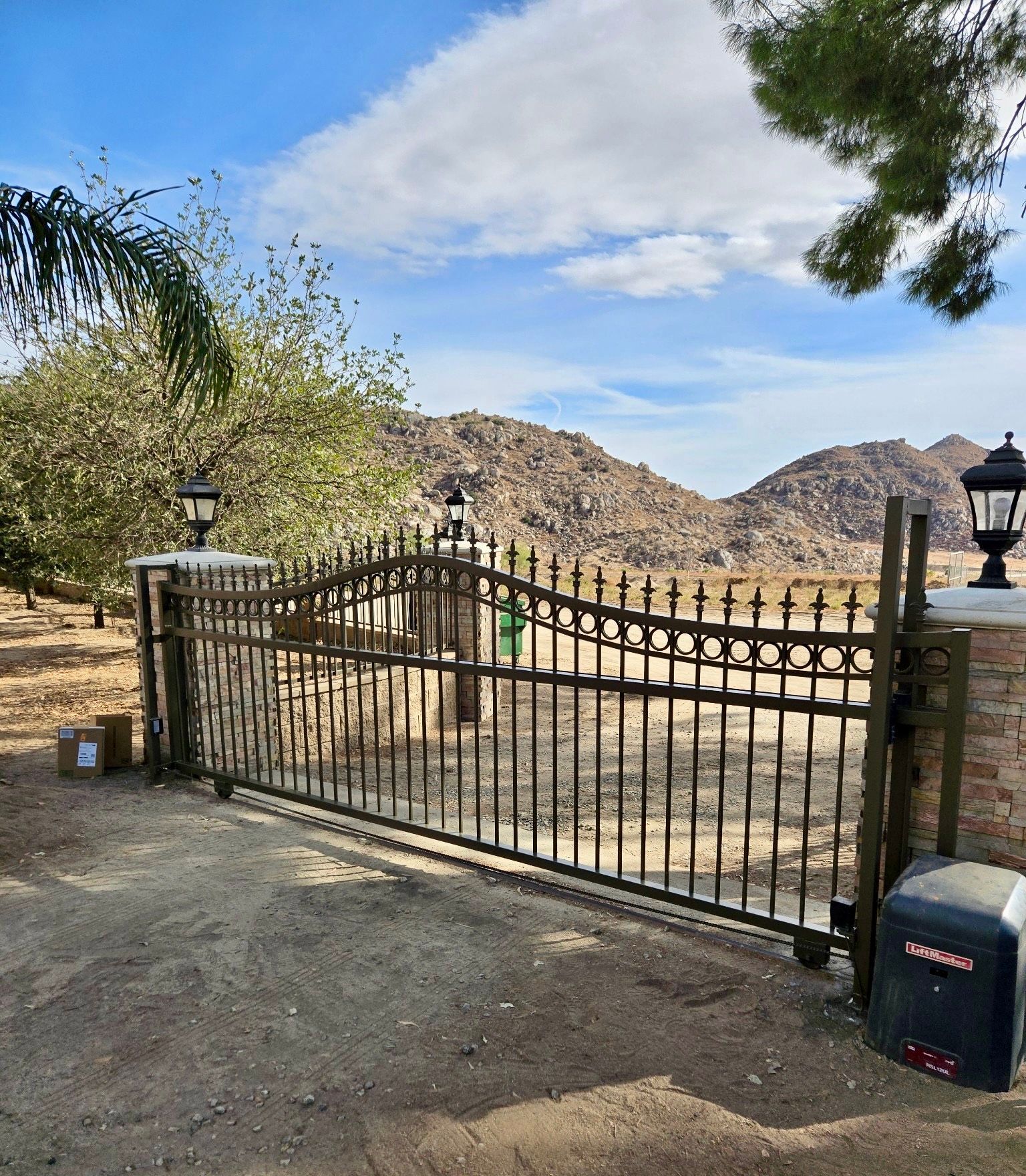 Black metal gate with brick pillars, in front of a mountain range under a blue sky.