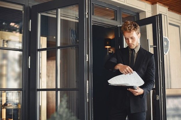 Man in suit holding papers, standing in doorway, looking down.