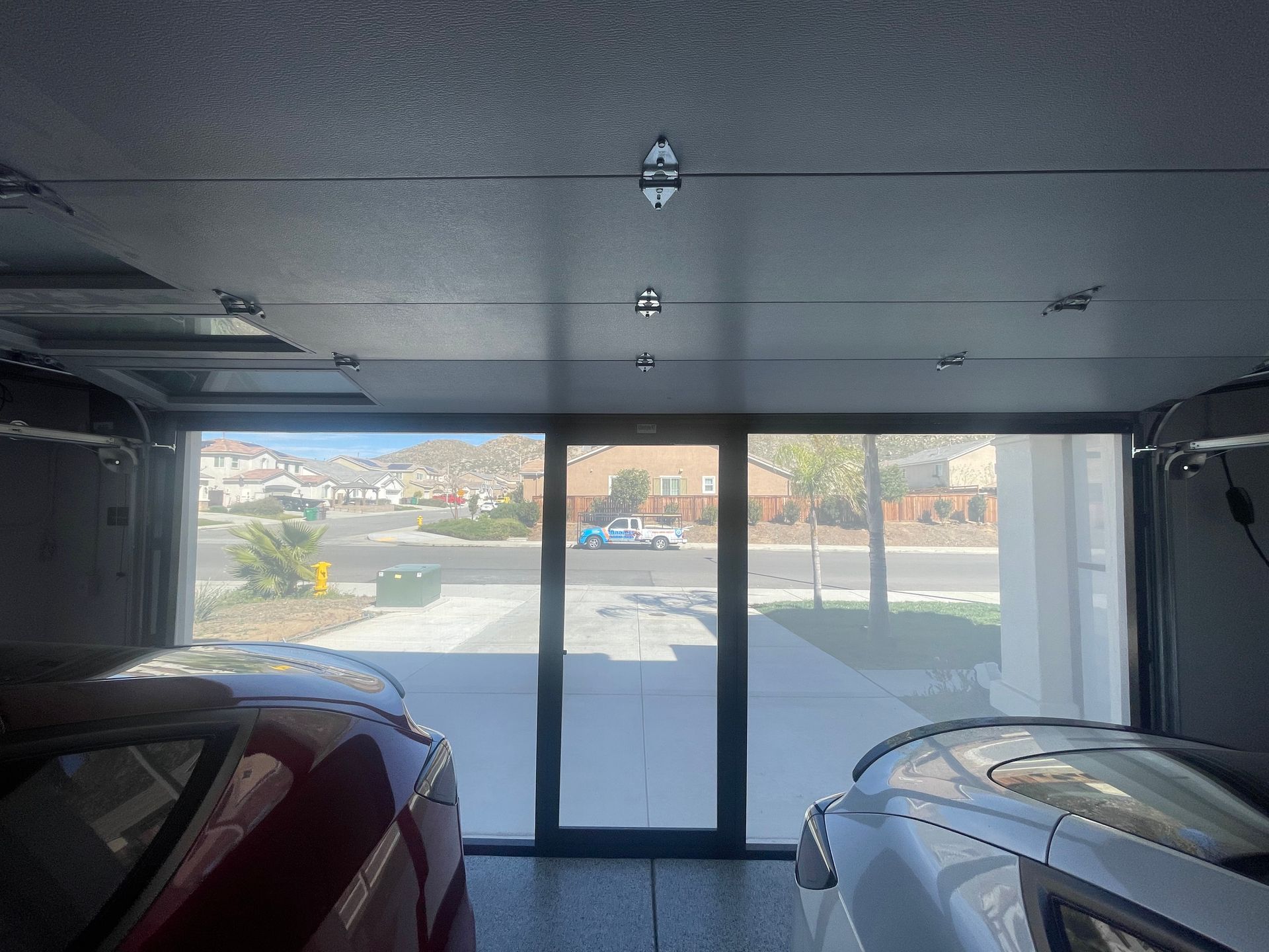 Two cars are parked in a garage with a large glass door.