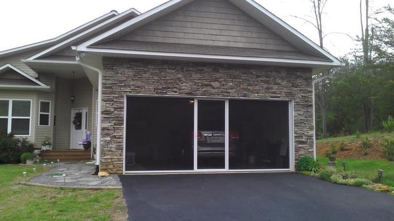 Garage with stone facade and screened doors, black asphalt driveway.