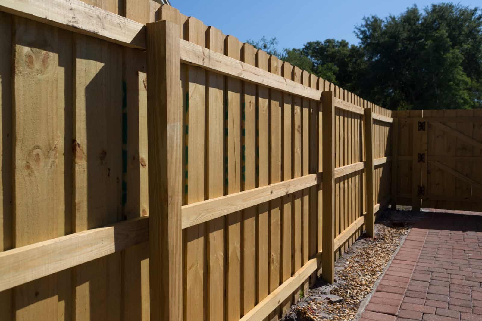 A wooden fence along a brick driveway with trees in the background