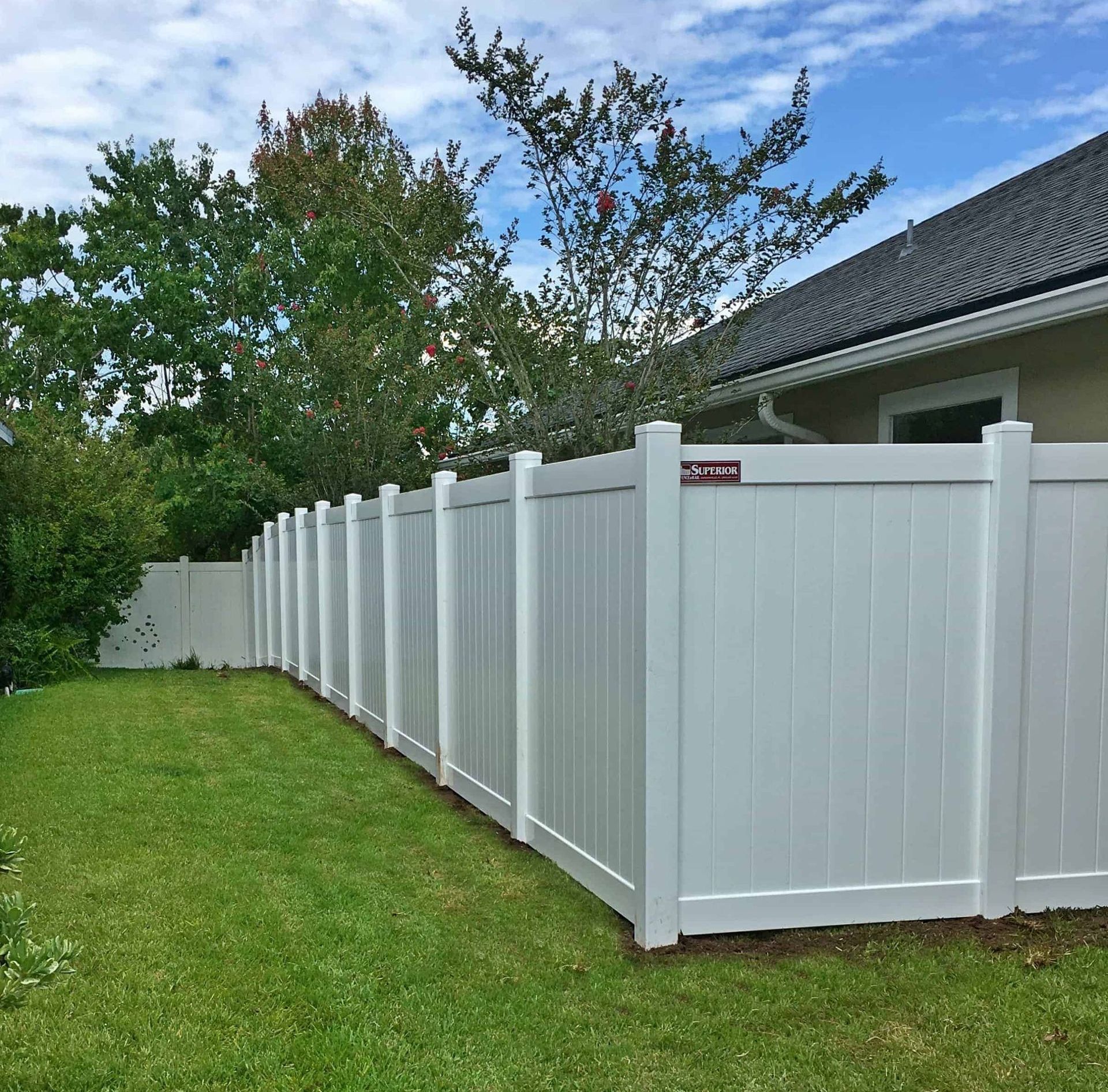 A white Vinyl fence surrounds a lush green yard in front of a house.