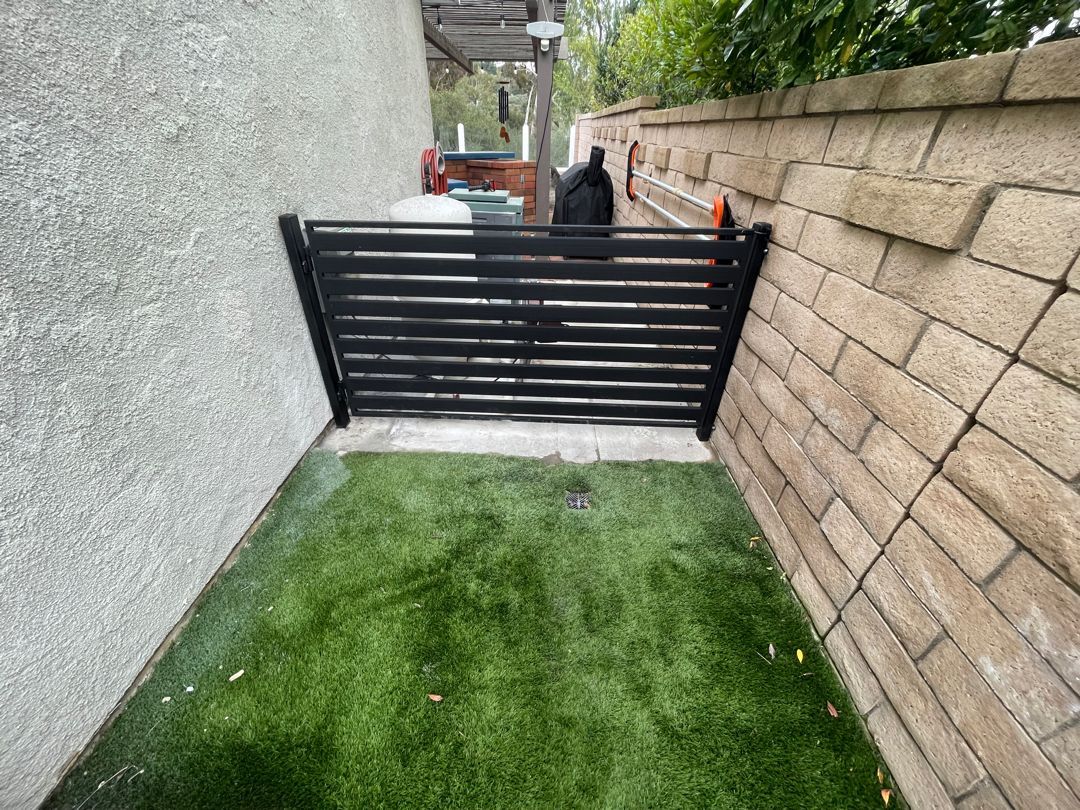 A brick wall with a fence and a lawn in front of it.