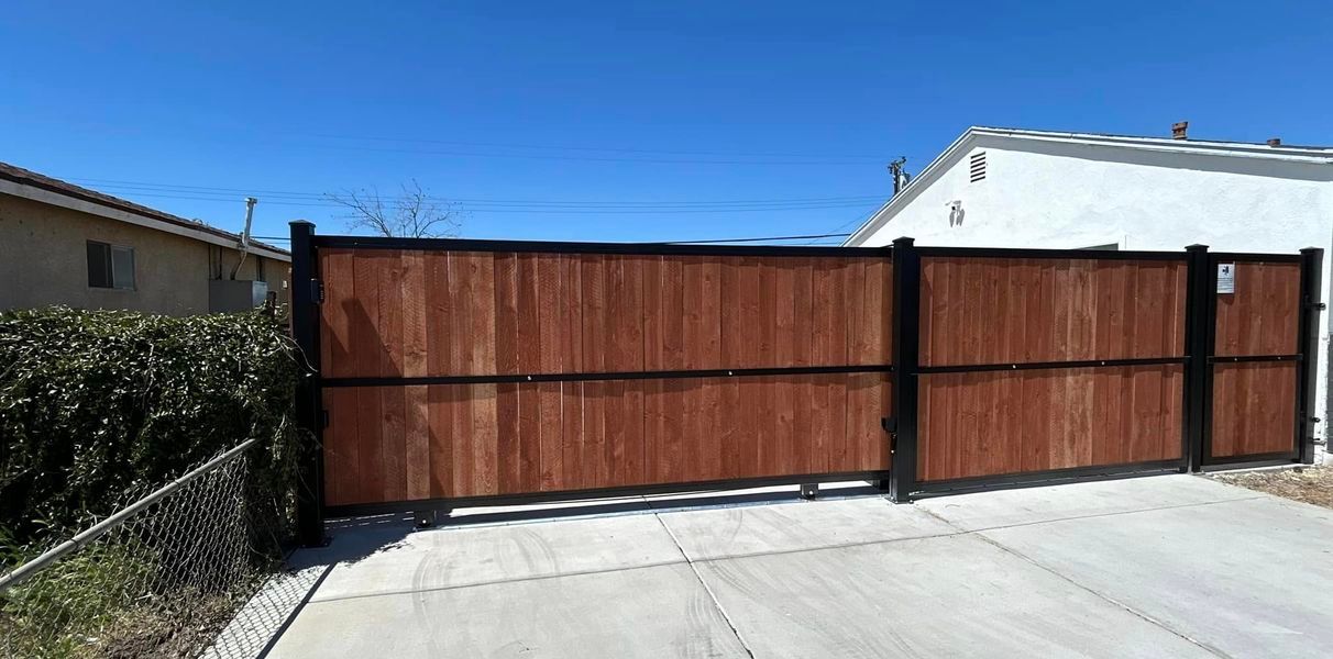 A wooden gate is sitting in the middle of a driveway next to a house.