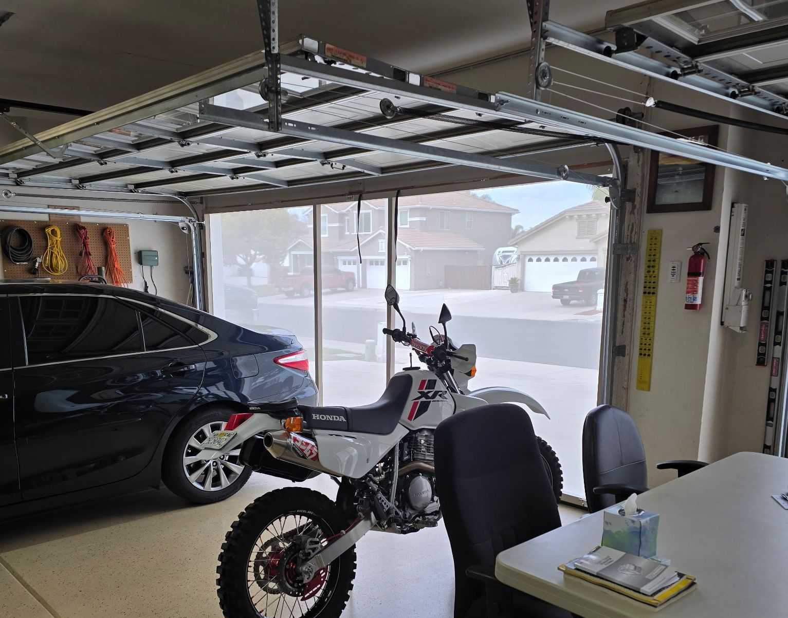 A garage with a motorcycle, car, and open door view to a residential street.