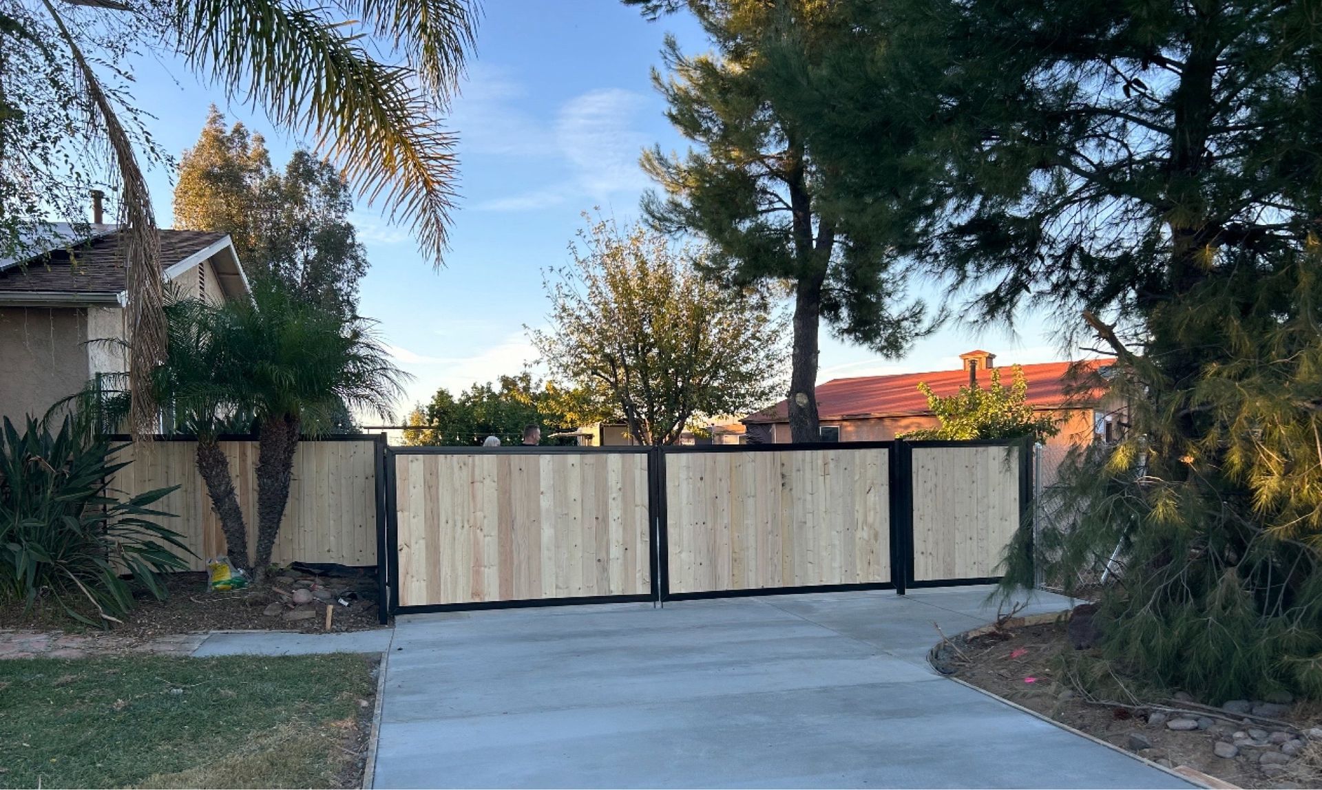 A wooden fence surrounds a driveway leading to a house.
