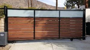 A wooden sliding gate with a glass divider is sitting on top of a concrete driveway.