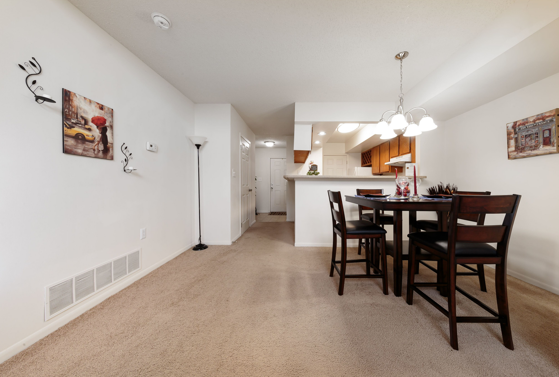 Open-concept dining area with a round dark wood table and four chairs, kitchen in the background.