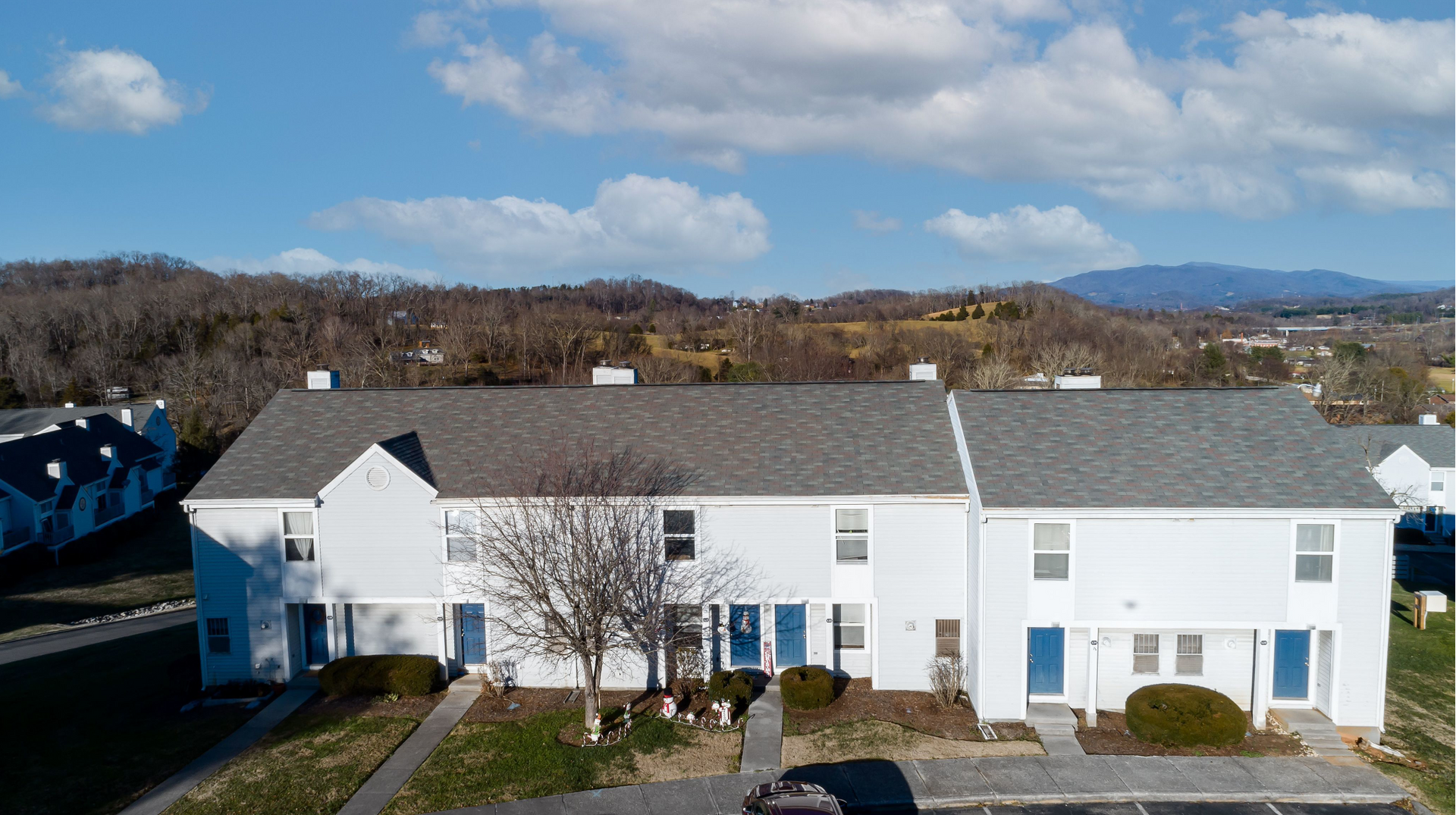 An aerial view of white townhouse-style apartment buildings with blue doors and manicured landscaping.
