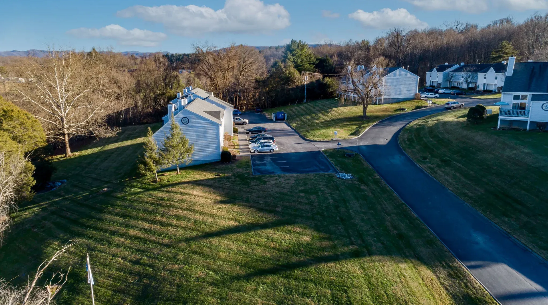 Aerial view of a suburban apartment community with white buildings, green lawns, driveways, and a curved road.