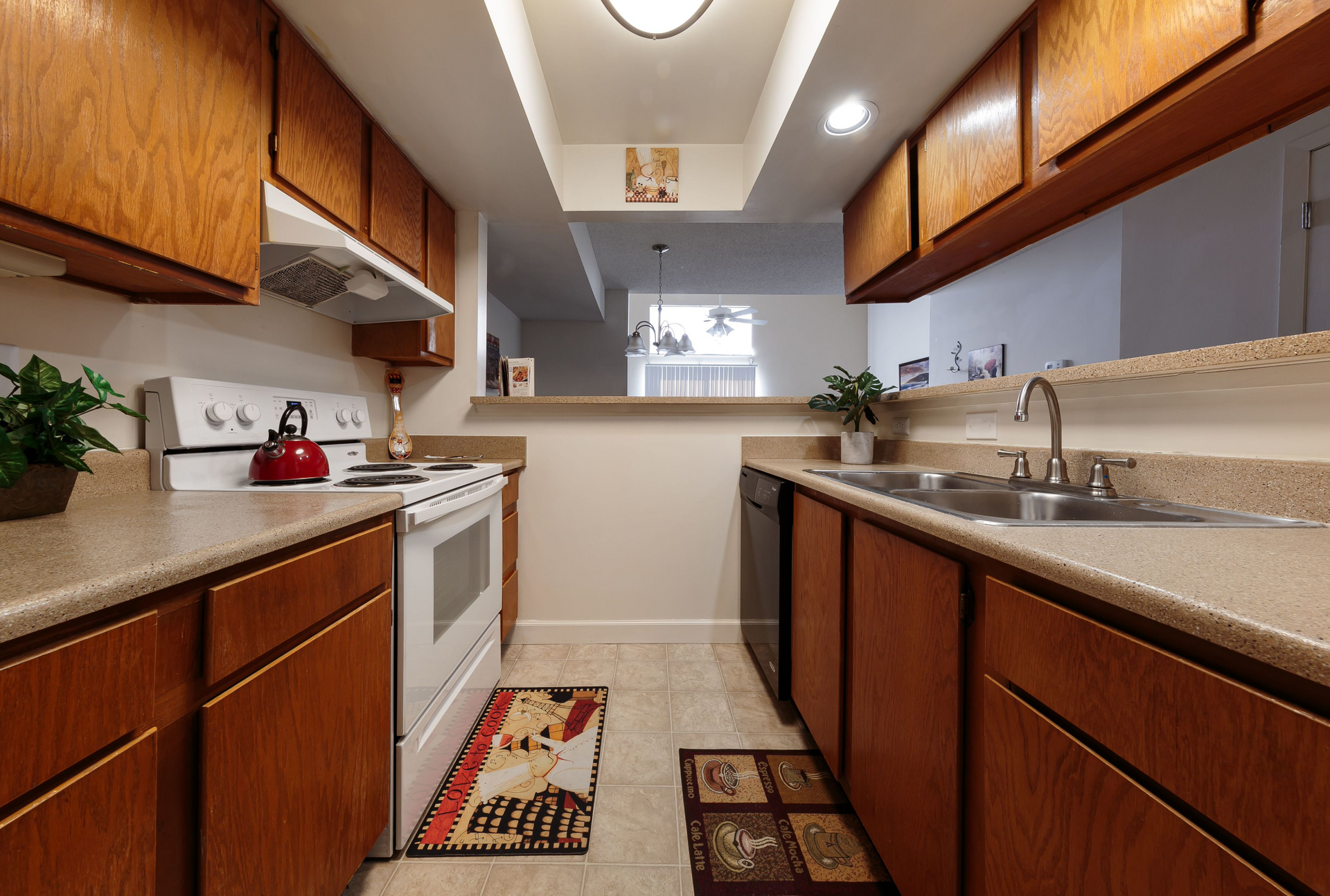 Galley-style kitchen in an apartment with wood cabinets, beige countertops, a white stove, and a double sink.