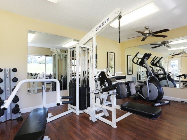 Bright home gym with treadmill, weight machine, benches, mirrors, and ceiling fan