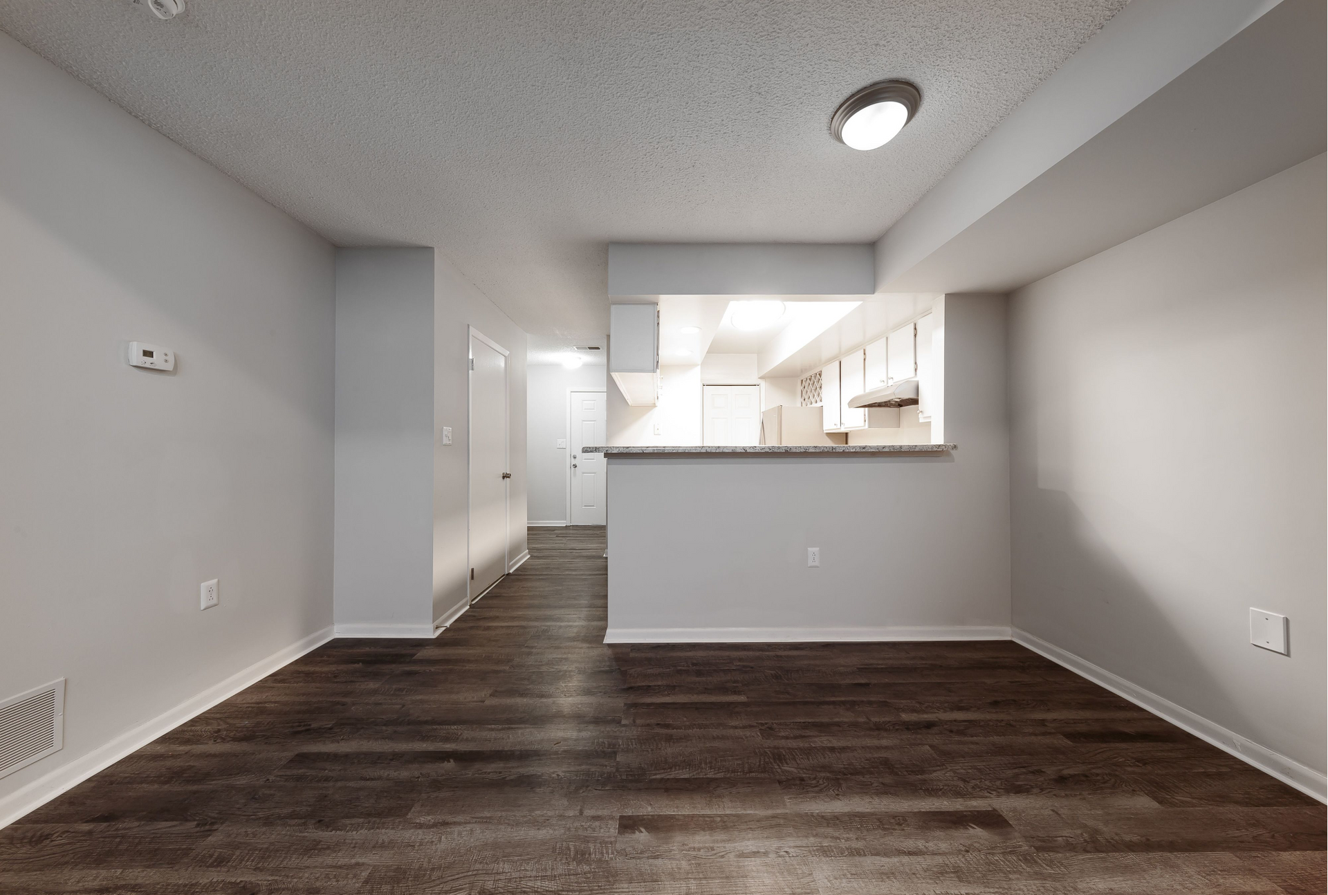 Living area with dark wood flooring and open kitchen pass-through.