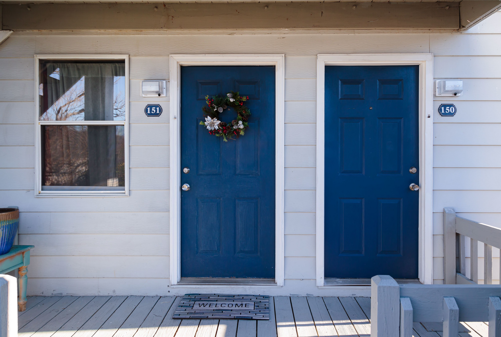 Exterior of a duplex-style building with two blue doors and a wreath on the left door.