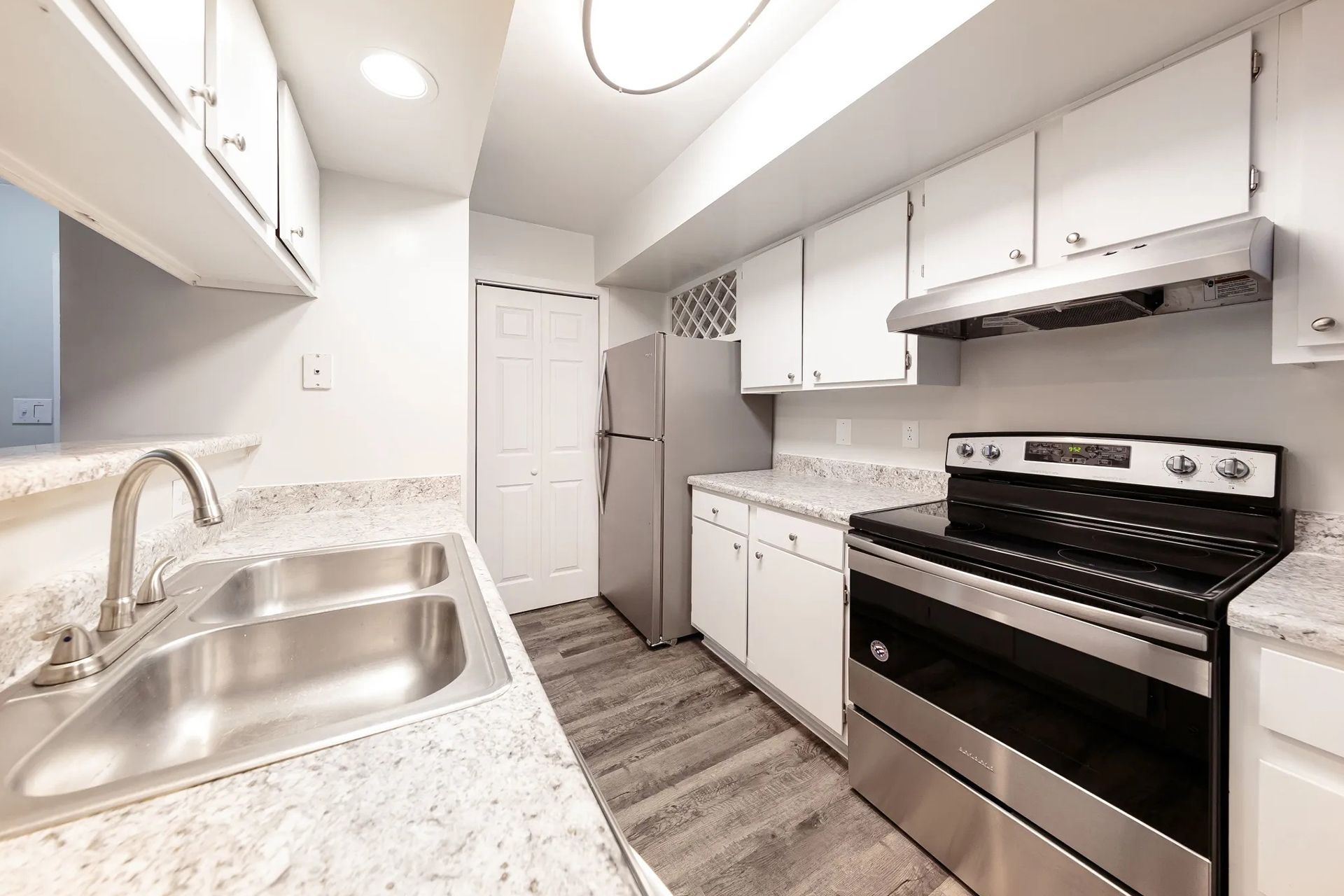 Bright galley kitchen with white cabinets, stainless steel appliances, and granite countertops