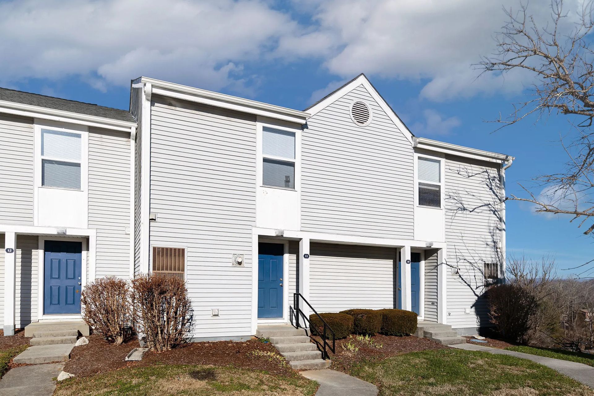 Row of apartments with light siding, blue doors, and a cloudy sky at Sterling Hills in Johnson City, TN.