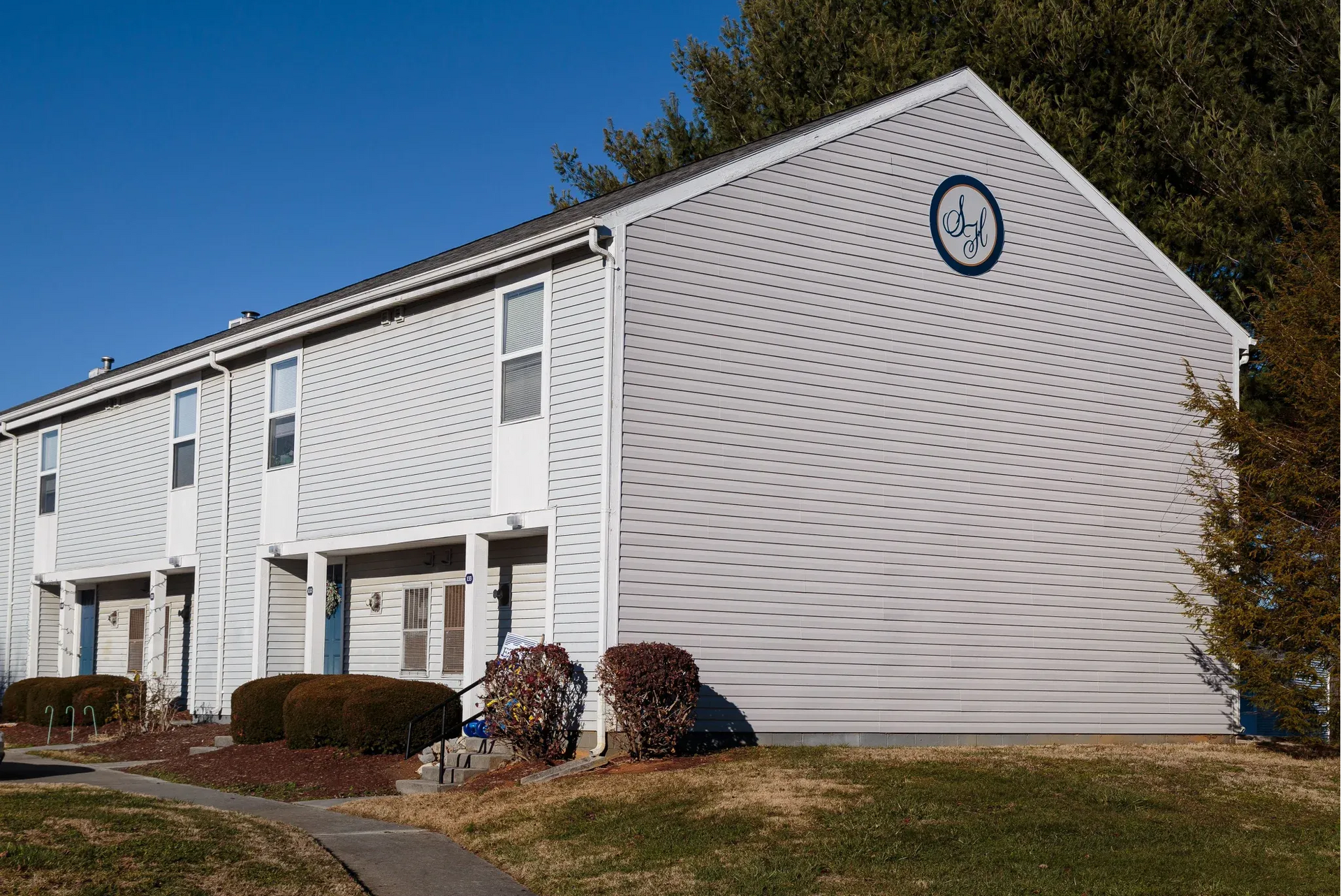 White two-story apartment building with a round logo on the front gable.