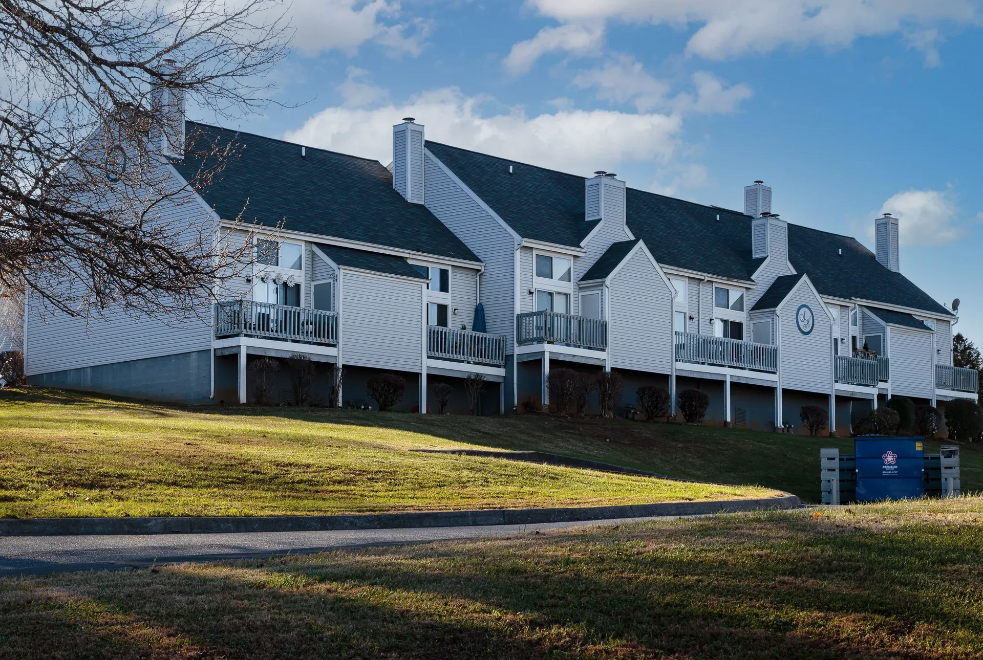 Exterior view of white, multi-unit apartment buildings with balconies on a grassy slope.
