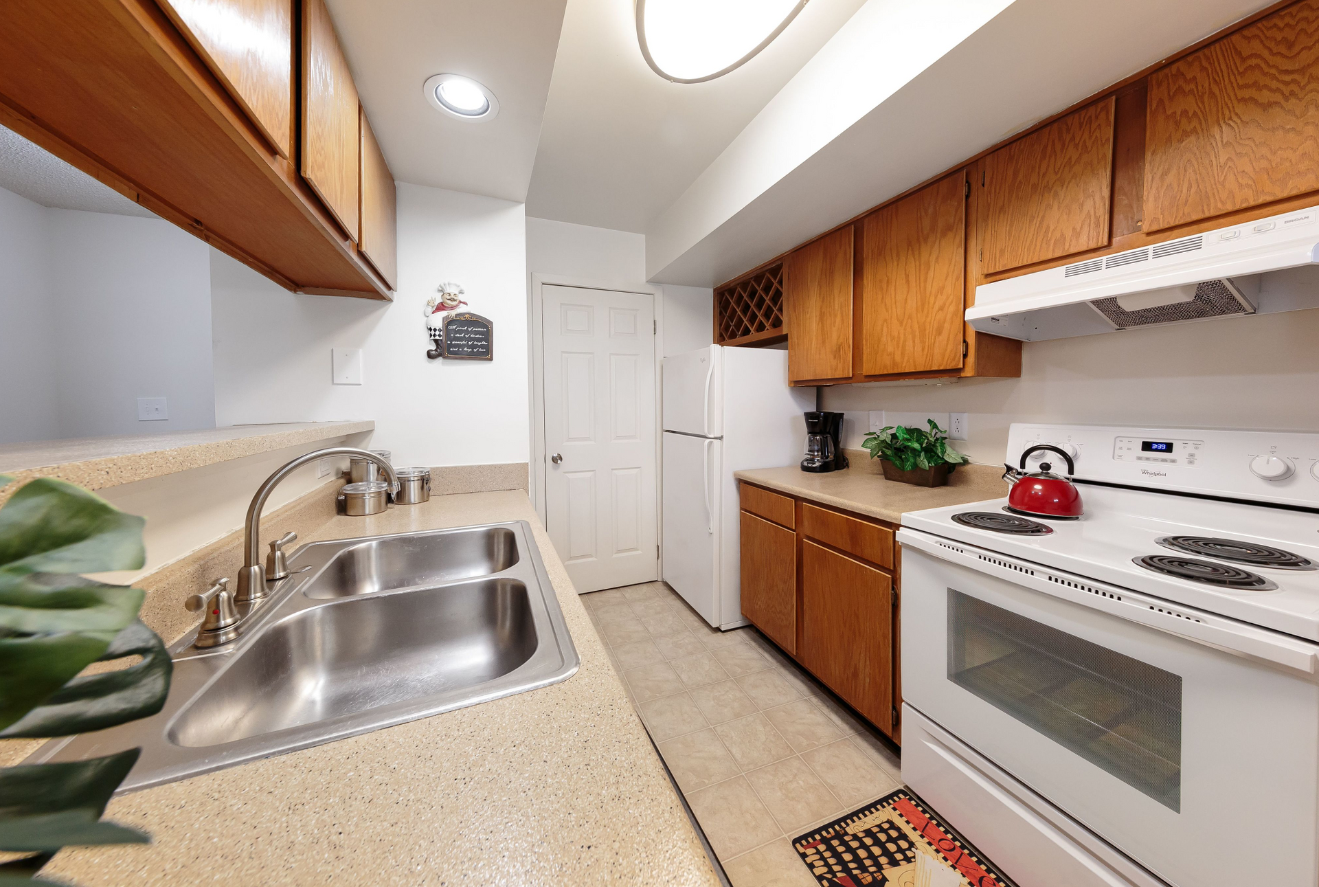 Kitchen area in an apartment with double sink, beige countertops, wooden cabinets, and white appliances.