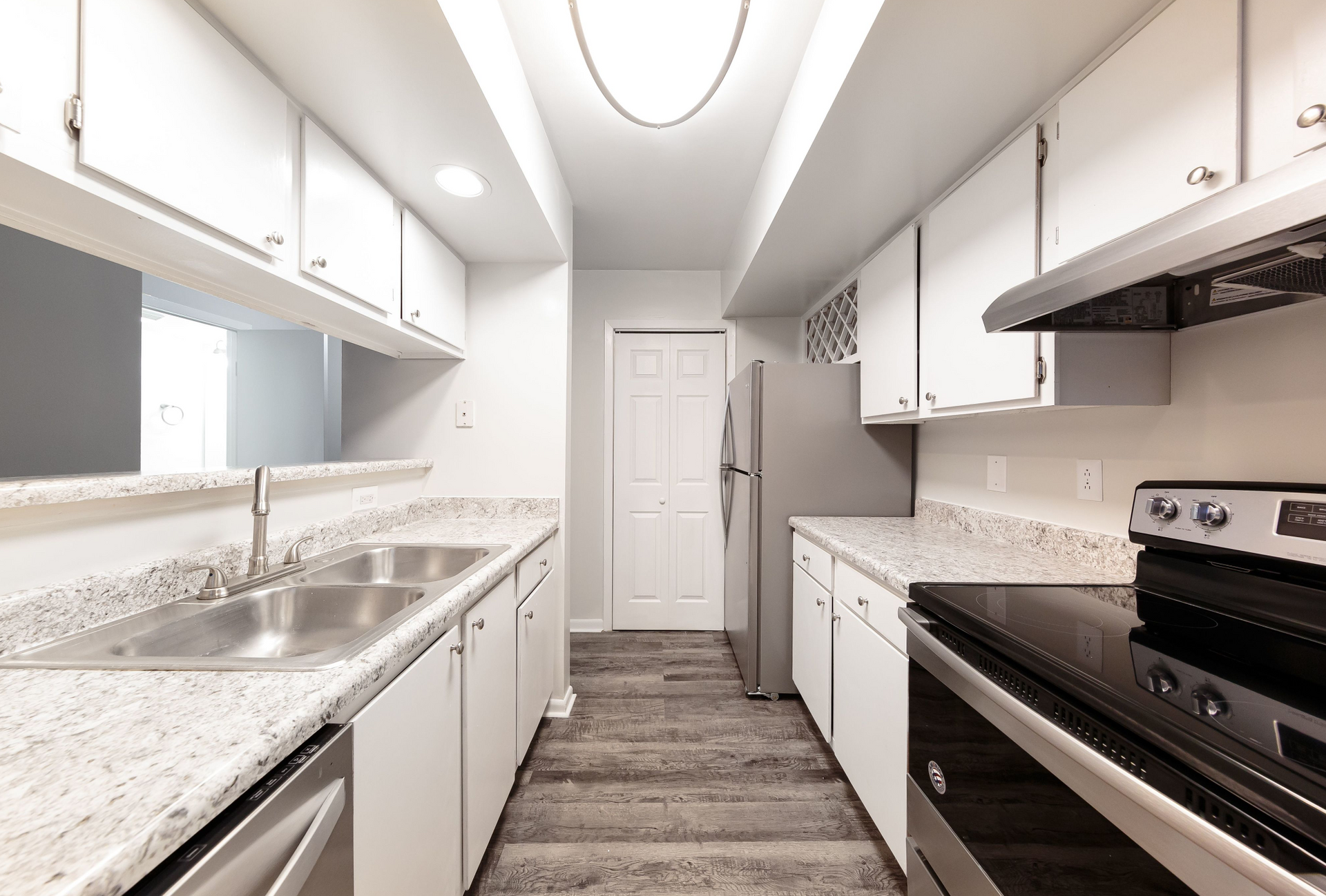 Bright galley kitchen with white cabinets, granite counters, a double-basin stainless sink, and stainless appliances.