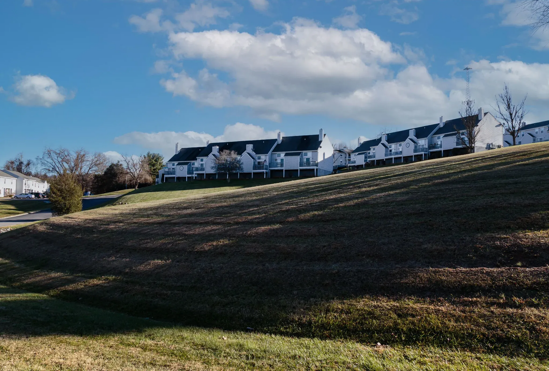 Exterior view of a white apartment complex on a grassy hill under a blue sky.