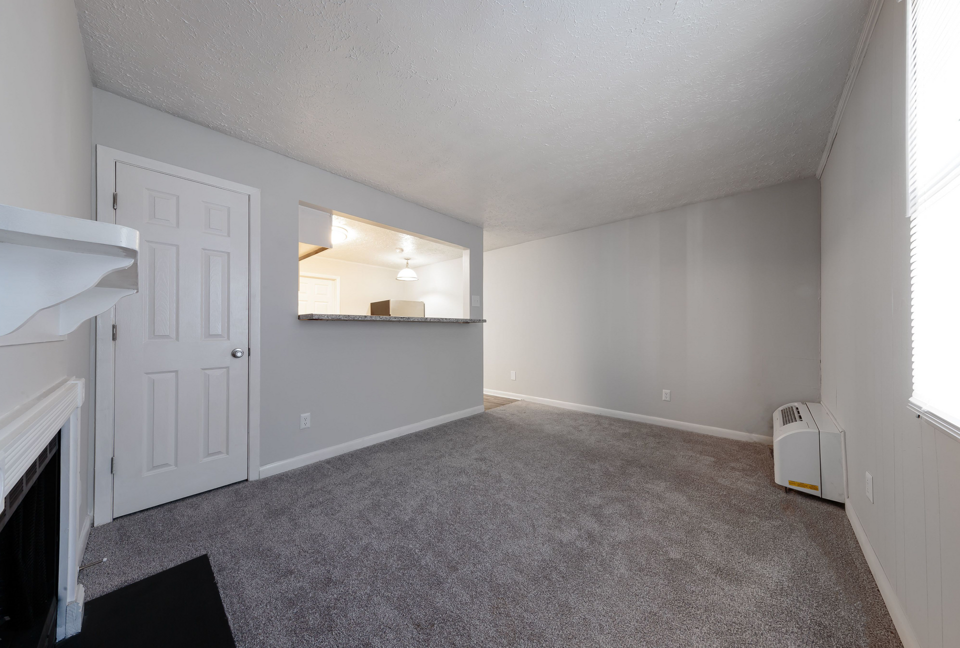 Living room with gray walls, carpet, a fireplace on the left, and a kitchen pass-through window.