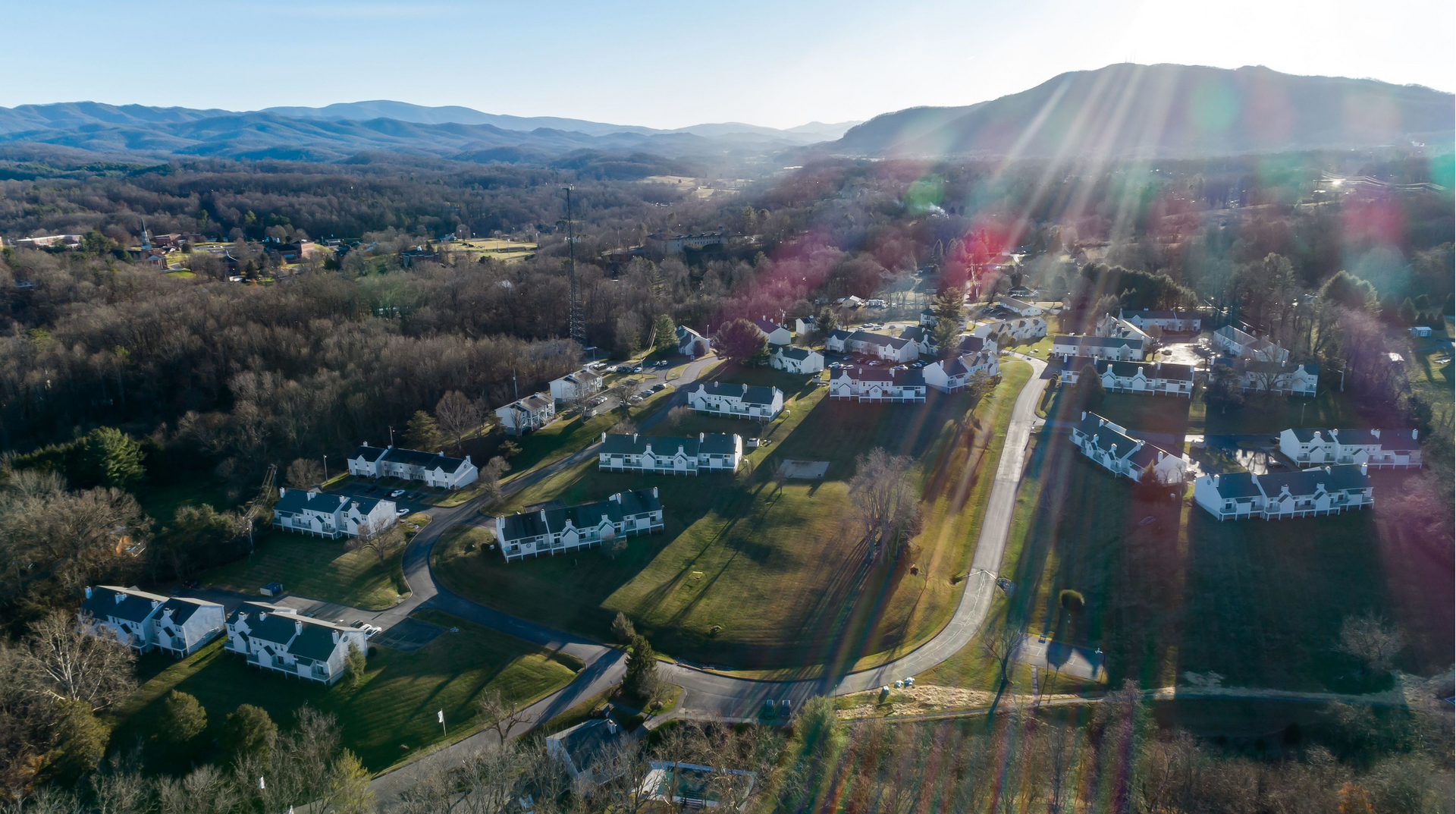 Aerial view of a suburban apartment community with curved roads, white buildings, and a mountain backdrop.