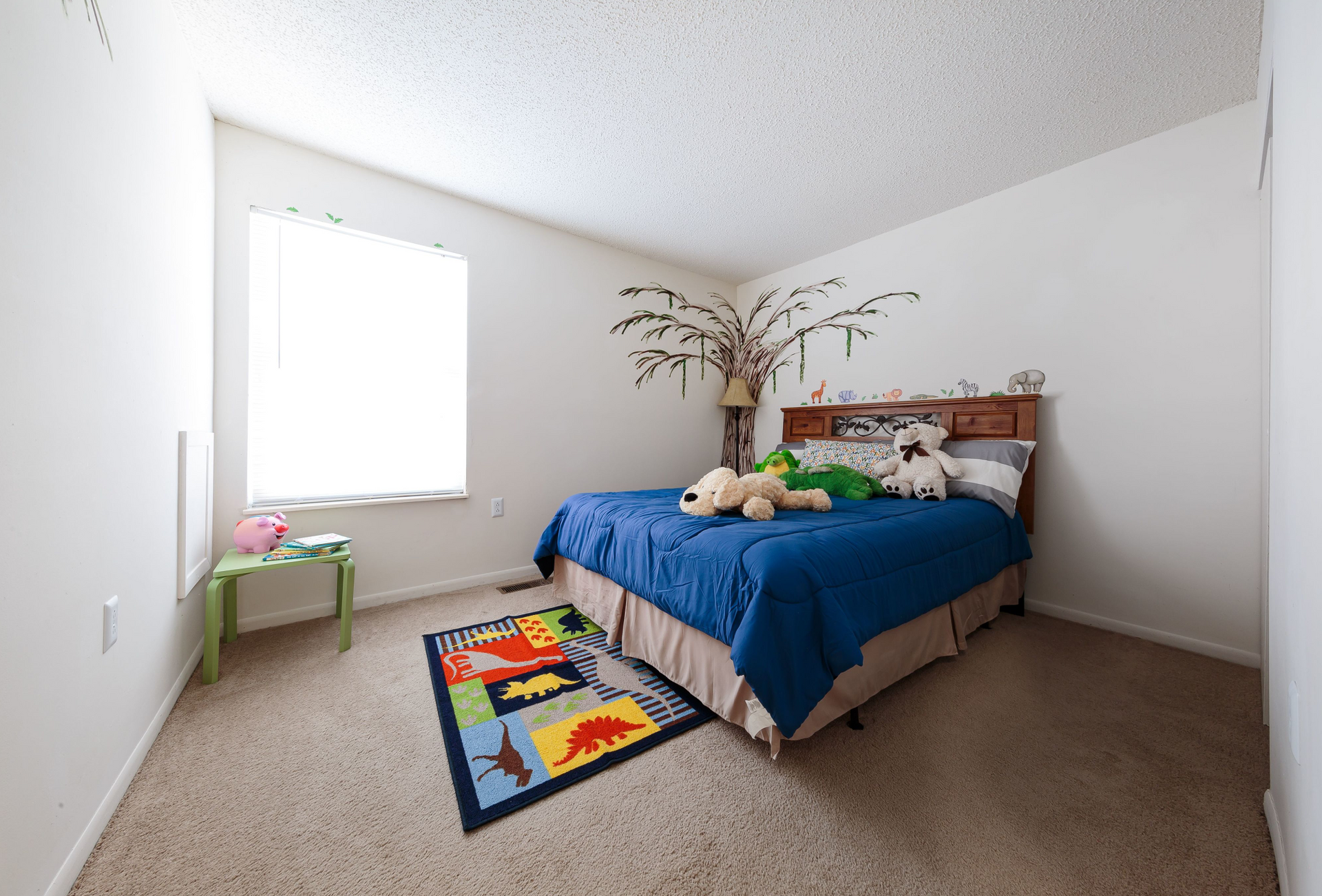 Child's bedroom with a blue comforter, stuffed animals, and a window.