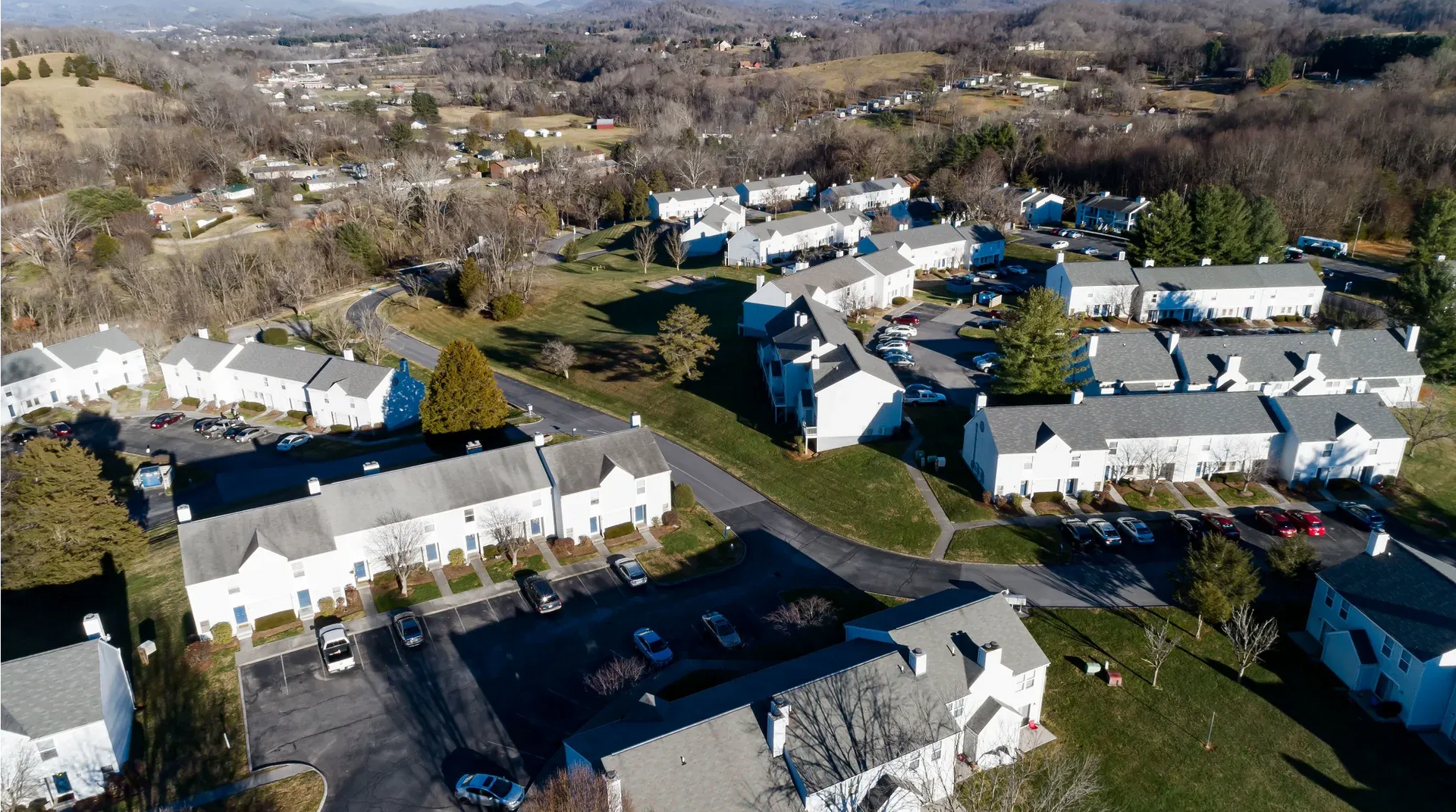 Aerial view of a white apartment complex with multiple buildings, parking lots, and green lawns.