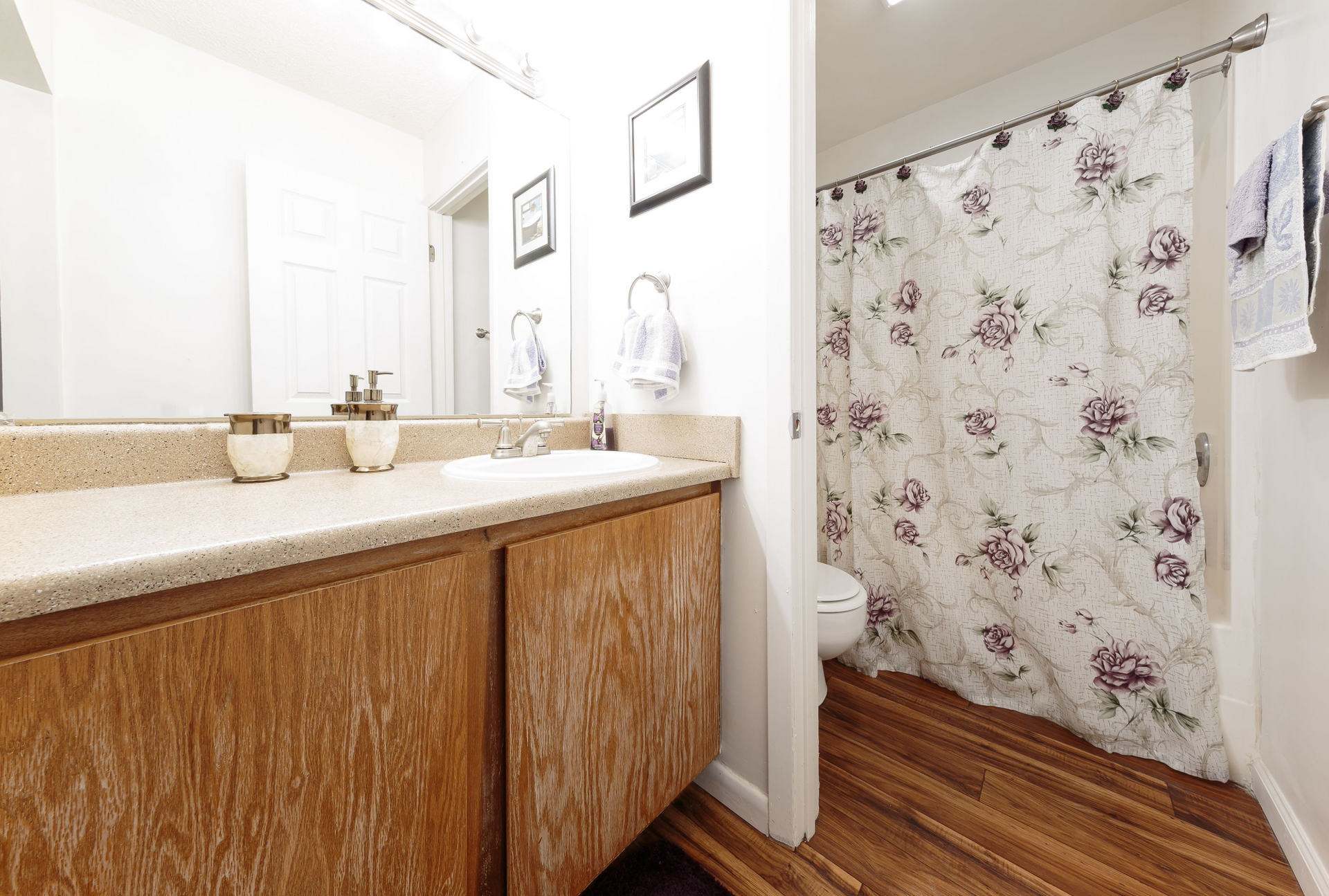 Bathroom with a wood vanity, beige countertop, and floral shower curtain.