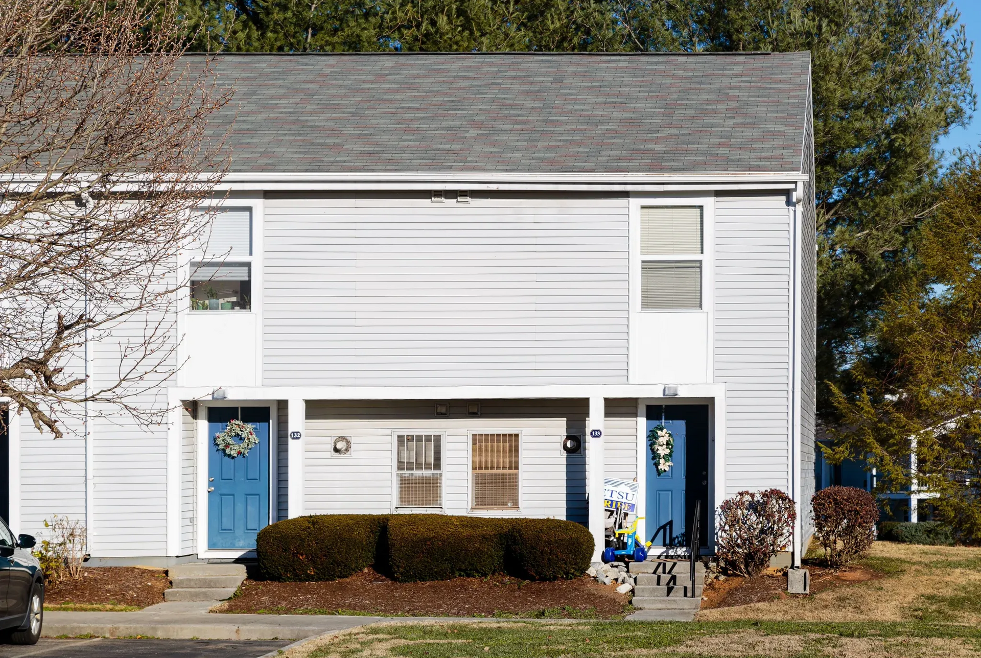 Exterior view of townhouse-style multifamily building with two blue entry doors and shrubbery.