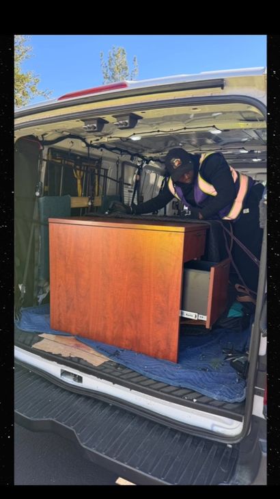 Two people loading a wooden piano into the back of a van