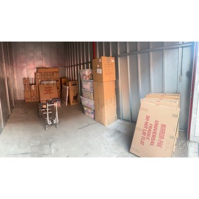 Storage container with stacked cardboard boxes and a hand truck on a concrete floor